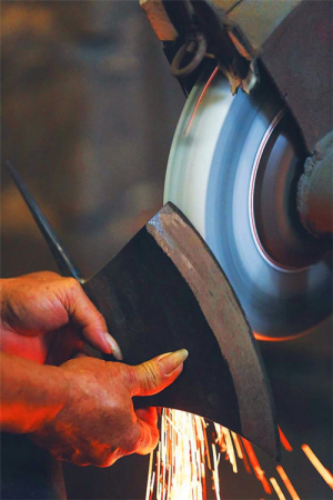 鐵菜刀的鋒口在砂輪的打磨下，漸露鋒芒。