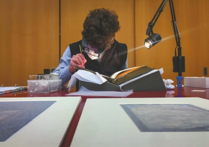 一名修復師正在聚光燈下修復一本印度的古書。