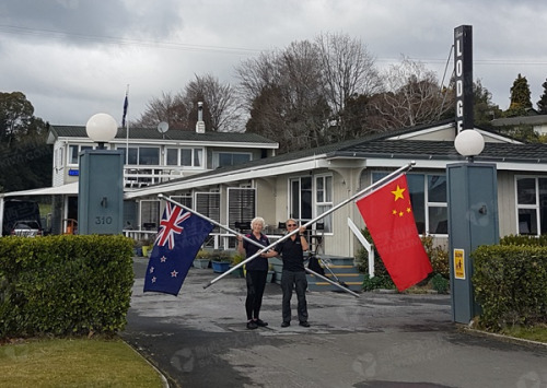  Jenkins夫婦在旅館門口手持中新兩國國旗，拍下這張照片。（新西蘭天維網(wǎng)）