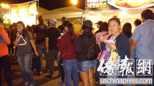 圣蓋博教會路餃子攤亭一個挨一個，每個攤亭前都大排長龍，圣蓋博居民鄧曉玲女士(右二)一邊吃餃子一邊排隊。(僑報記者高睿攝)