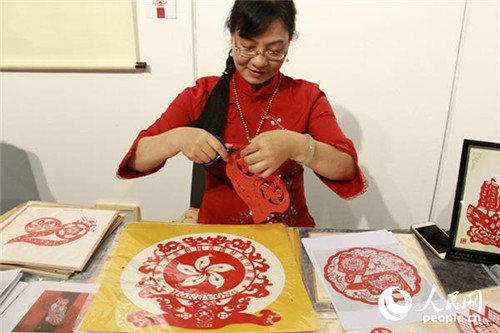 潮陽(yáng)剪紙傳承人魏惠君現(xiàn)場(chǎng)展示，她的面前就擺放著專為此次展覽設(shè)計(jì)的“20”(左一)和區(qū)徽(左二)圖樣。(攝影：吳玉潔)