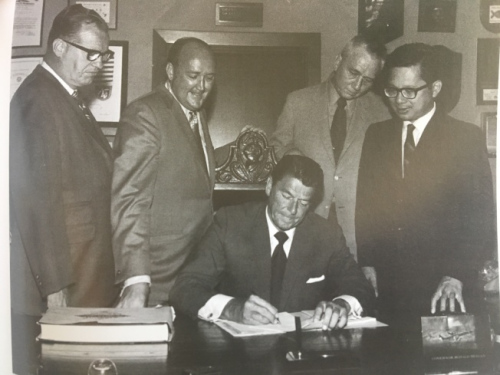 當(dāng)時(shí)還是州長(zhǎng)的里根(Ronald Reagan)簽署譚卓?jī)x(右一)的“教育補(bǔ)償計(jì)劃”提案。(圖片來源：譚卓?jī)x提供)