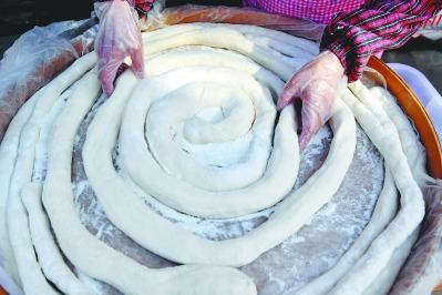 林傳星的妻子孫巧瑤把麥芽糖包裹酥脆的花生等配料揉搓拉成條狀，再用剪子斜剪成塊狀。