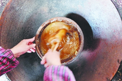 熬制糖汁需要土灶恒溫，林傳星的妻子孫巧瑤要守在旁邊片刻不停地攪拌翻動，直至呈深褐色的膠狀。