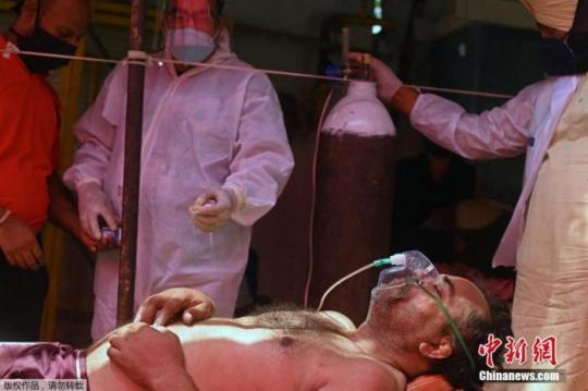 資料圖：當(dāng)?shù)貢r(shí)間4月26日，印度加茲阿巴德，一名新冠患者在路邊搭建的帳篷內(nèi)吸氧。