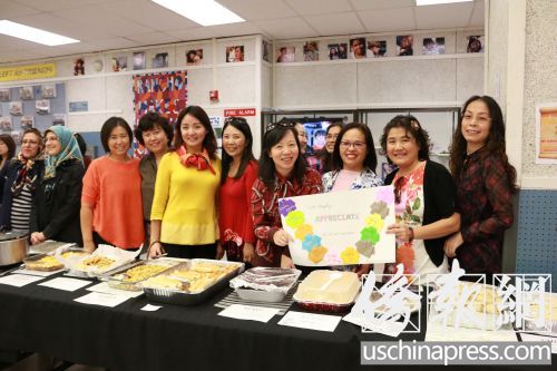 華裔家長手舉學(xué)生制作的感謝卡在美食分享臺前合影。(美國《僑報》/李幟一