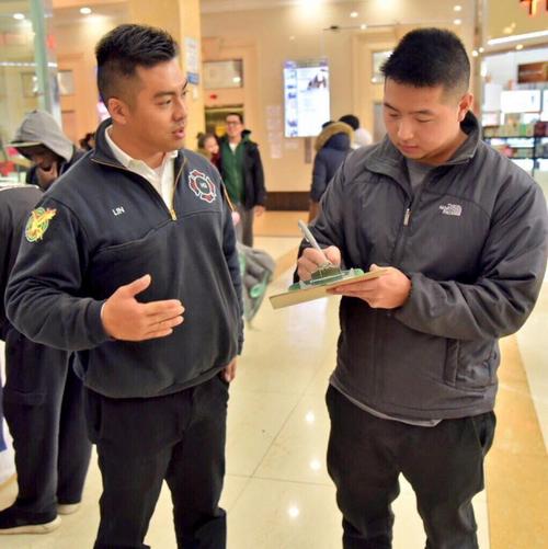 中國僑網(wǎng)林遠(yuǎn)文(左)在法拉盛的華人超市內(nèi)宣傳市消防局招聘項目。(美國《世界日報》)