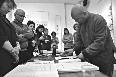 中國僑網(wǎng)魏中立在英國王儲傳統(tǒng)藝術(shù)學院展覽現(xiàn)場向觀眾講解水印木刻